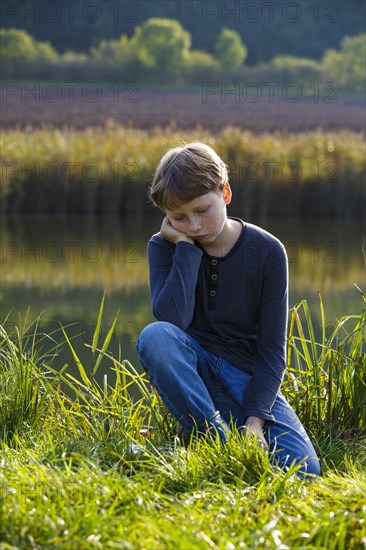 Sad boy sitting on a small lake