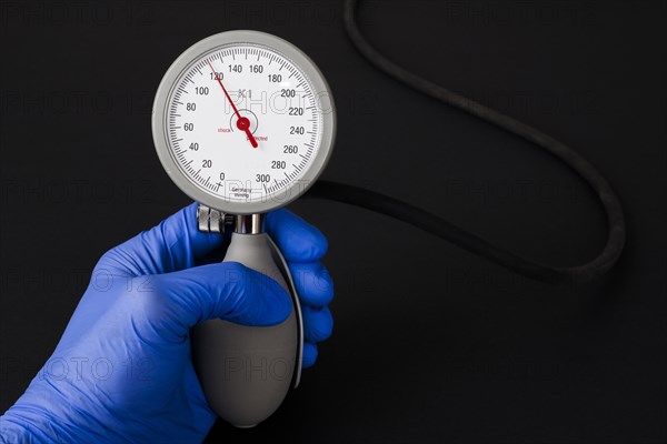 A hand with a blue medical glove is holding a sphygmomanometer