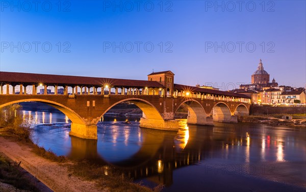 Illuminated bridge Ponte Coperto leads over the river Ticino with cathedral