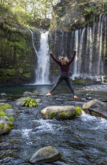 Young woman jumps into the air on a stone in a river