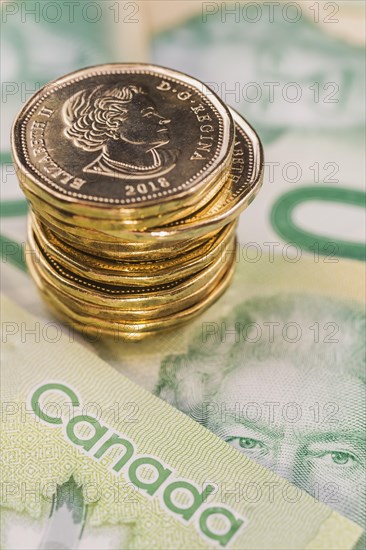 Stack of Canadian one dollar coins on top of Canadian twenty dollar bank notes with portrait of Queen Elizabeth II