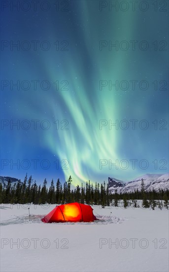 Northern Lights (Aurora borealis) above a red illuminated tent in winter