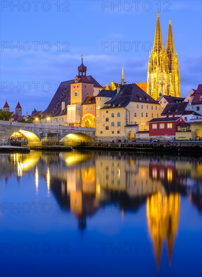 Illuminated Old Town with Stone Bridge and Cathedral reflected in the Danube at dusk