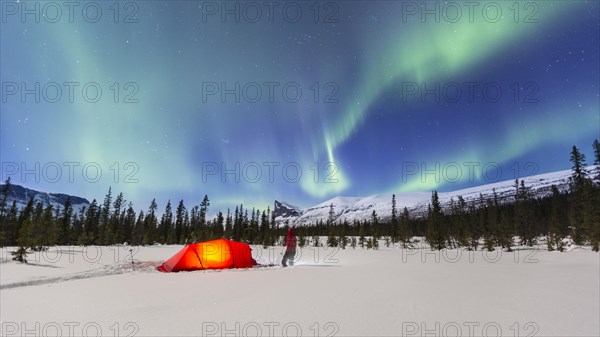 Northern Lights (Aurora borealis) above a red illuminated tent in winter