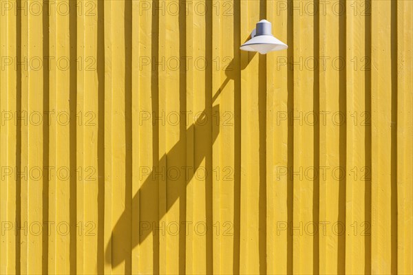 Lamp on a yellow beach hut casting a long shadow