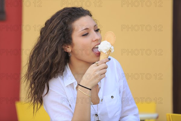 Teenager eating ice cream from a cone on the terrace of an ice cream parlour