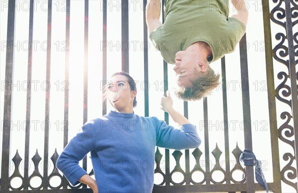 Young man trying to impress indifferent girl by hanging upside down on an iron gate