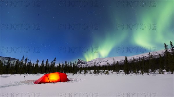 Northern Lights (Aurora borealis) above a red illuminated tent in winter