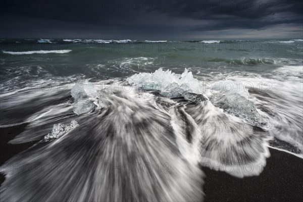 Pieces of ice on black beach lapped by the sea