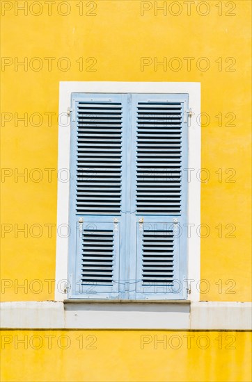 Yellow plastered wall with closed bright blue wooden shutters