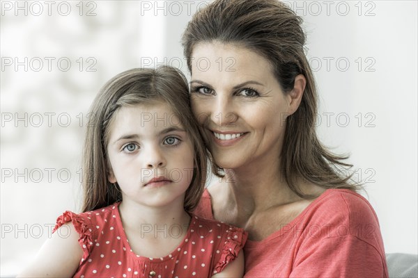 Mother and daughter sit together on the couch and look into the camera
