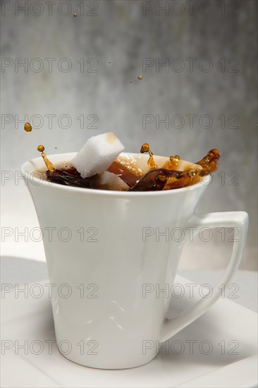 Two sugar cubes falling into a cup of coffee