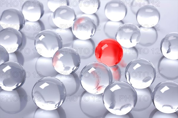 A red glass ball amidst many colourless glass balls