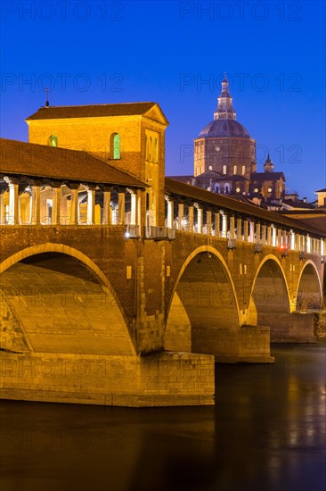 Illuminated bridge Ponte Coperto leads over the river Ticino with cathedral