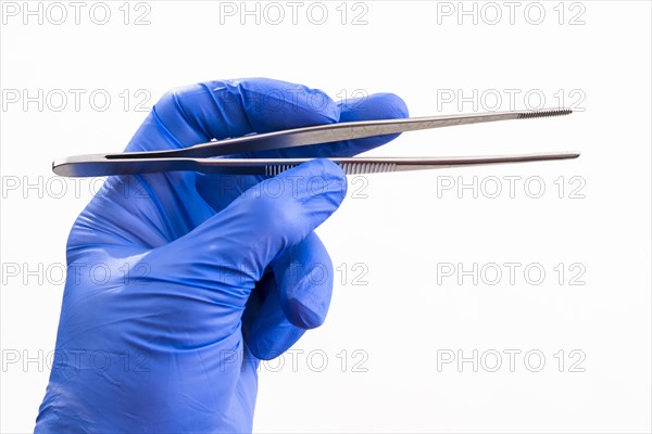 A hand with a blue medical glove is holding tweezers