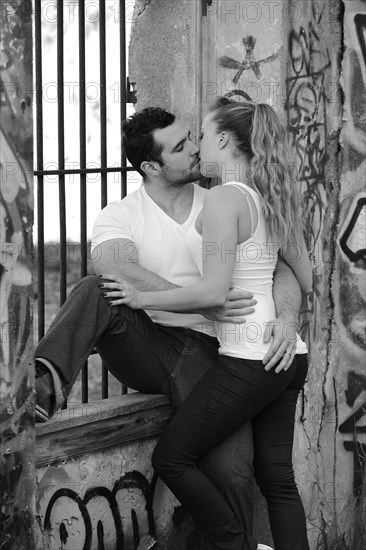 Young couple kissing at a barred window in a ruined building covered in graffiti