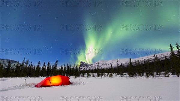 Northern Lights (Aurora borealis) above a red illuminated tent in winter