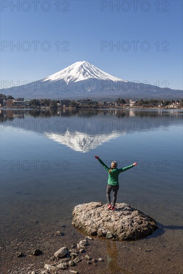 Young woman stands on stone in the water and stretches arms into the air