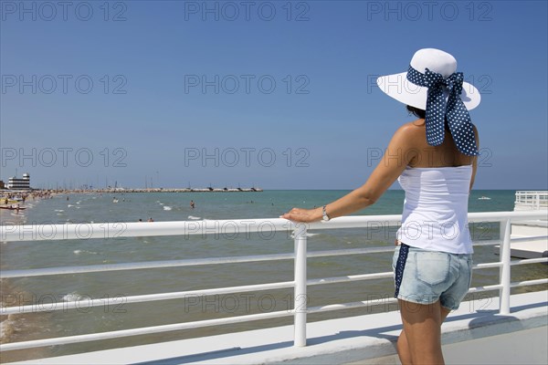 Woman with hat standing at railing on the beach