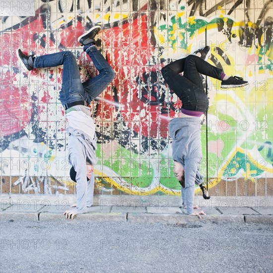 Young man and woman doing handstand in front of grafitti wall in urban area