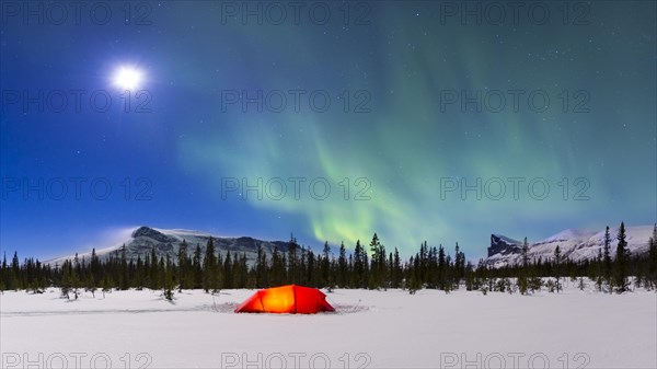 Northern Lights (Aurora borealis) above a red illuminated tent in winter