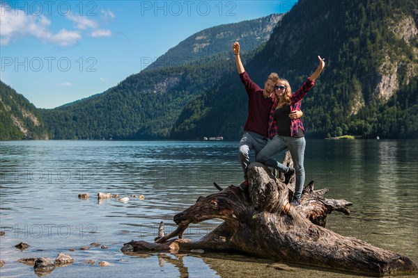 Young couple on a fallen tree trunk stretching their arms up in the air