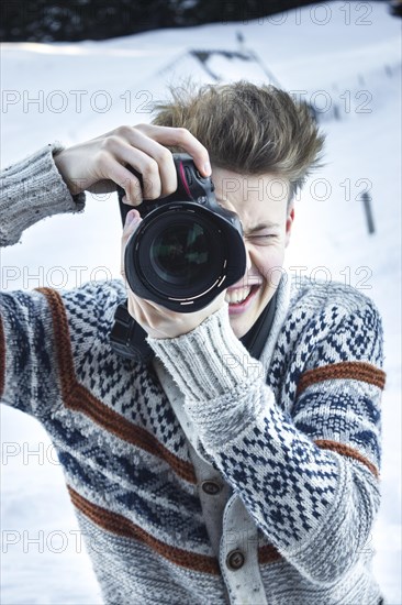 Young man in the snow taking a picture with a digital SLR camera