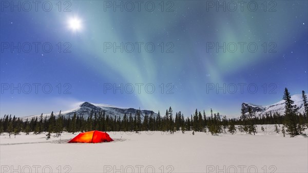 Northern Lights (Aurora borealis) above a red illuminated tent in winter