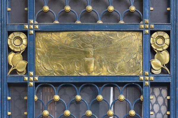 Gold-coloured relief of a bee at a wrought-iron gate around 1900