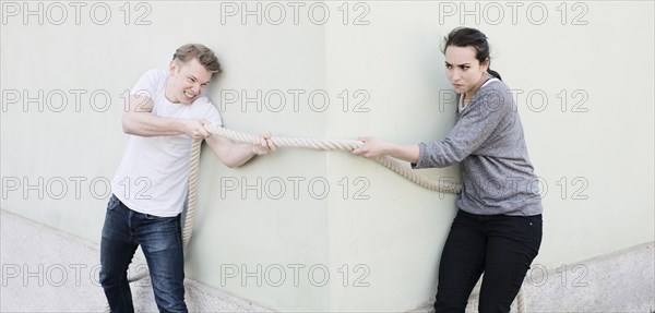 Angry couple pulling a rope from opposite sides of corner of house