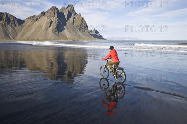 Woman riding a bicycle on the beach in front of Mt Vestrahorn near Hoefn