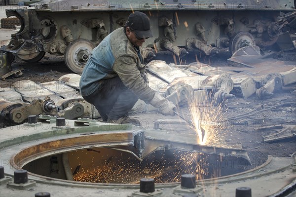 A man cutting up an armored vehicle type Marder with a torch