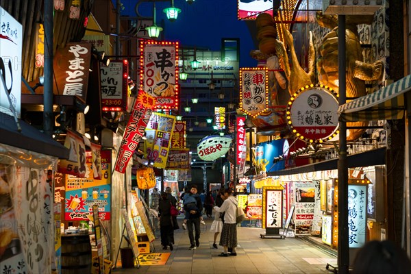 Many colorful neon signs in a pedestrian zone with shops and restaurants