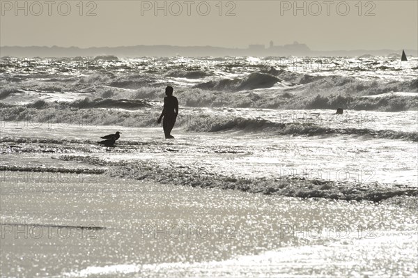 Woman in front of the surf of the North Sea in backlight