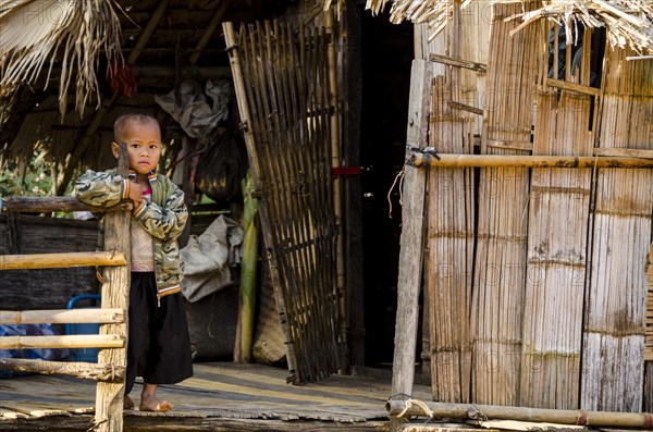 Child from the Lahu people standing outside a bamboo hut