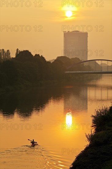 A canoeist on the Rhine-Herne Canal at sunset with Gasometer