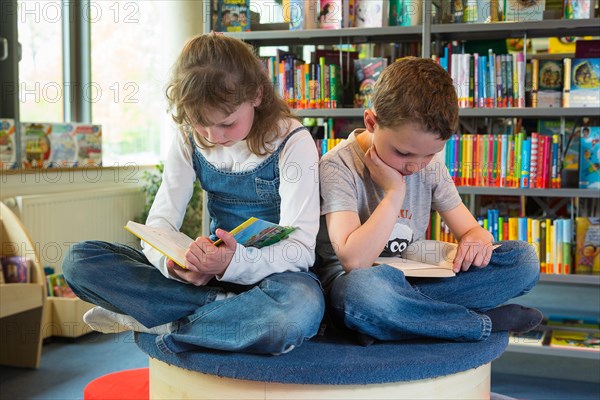 Two children reading reading books in a public library