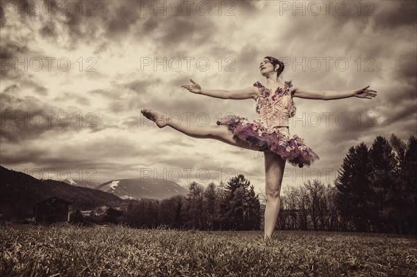 Ballerina wearing a tutu dances in front of a cloudy