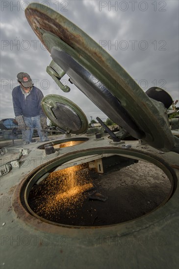 A man cutting up an armored vehicle type Marder with a torch