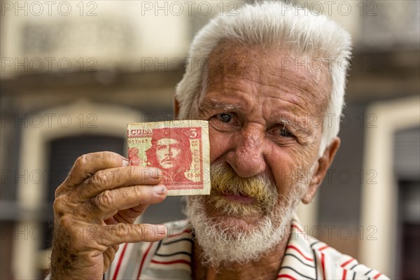 Elderly Cuban man holding a 3-peso bill with the portrait of Ernesto Che Guevara in his hand