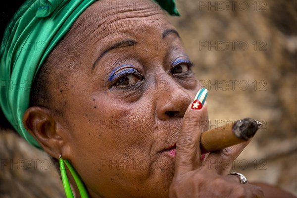 Senior Cuban woman with the Cuban flag painted on her fingernail smoking a Cuban cigar