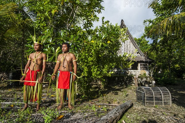 Two traditionally dressed men standing in front of stone money