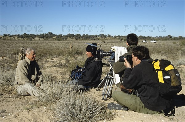 Sir David Attenborough with meerkat on shoulder being filmed for BBC series Life of Mammals