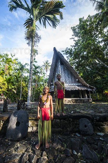 Two traditionally dressed boys standing in front of a traditional hut