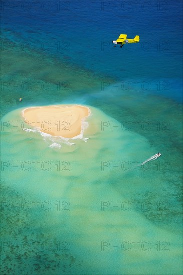 Small plane flying over coral reef with sand island