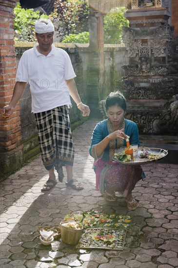 A woman during the daily ceremony of sacrificial offerings in front of a house