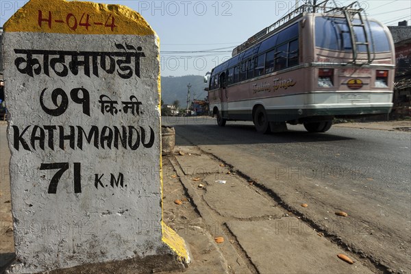 Milestone at the roadside with a Nepalese bus passing
