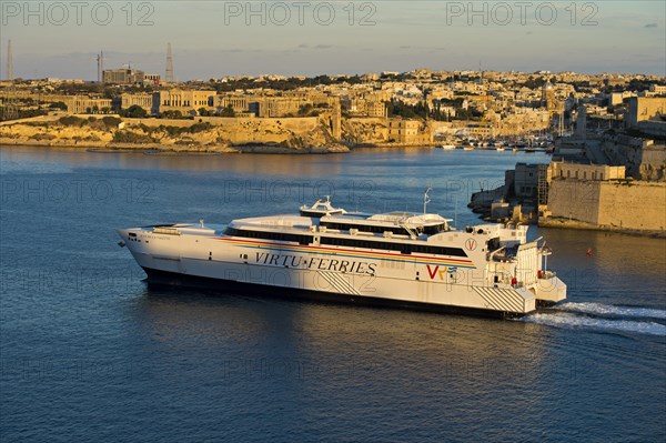 Jean de la Valette ferry of the Virtu Ferries shipping company passing the fortress Fort St. Angelo in the Grand Harbour