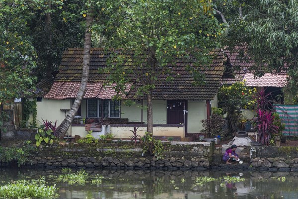 Woman washing the dishes in a canal in front of her house