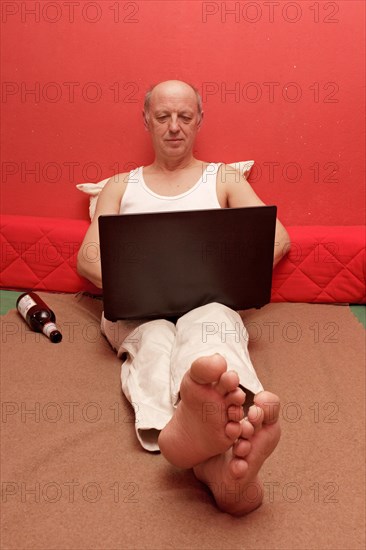 Man sitting up in bed with laptop and beer bottle